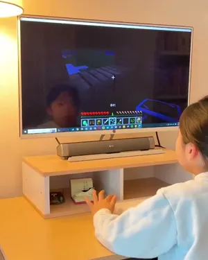 A child, seen from behind, playing Minecraft on a monitor at a desk