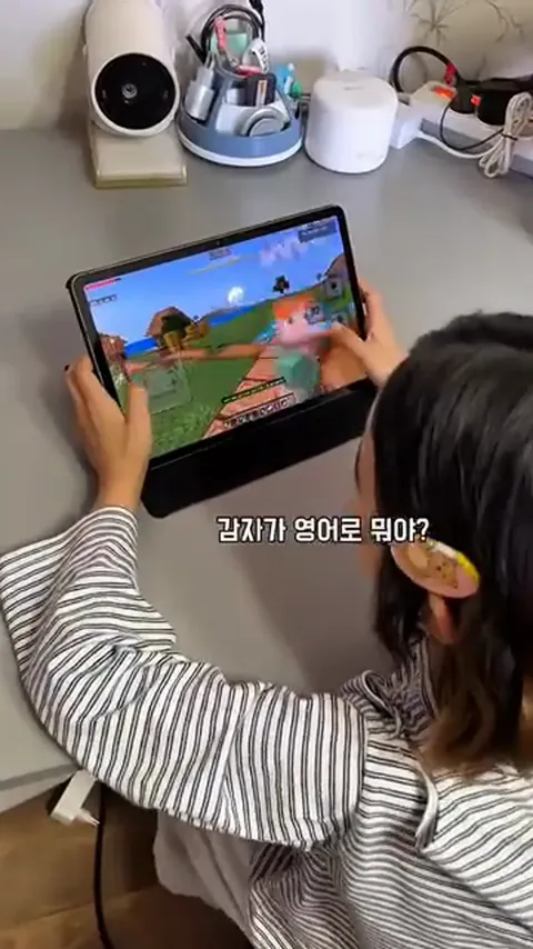 A child, seen from behind, playing Minecraft on a tablet and talking with Annie